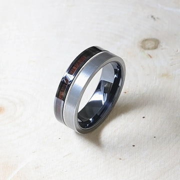 Angled view of the SLATE hybrid ring on a wooden surface, revealing black ceramic interior and brushed tungsten exterior