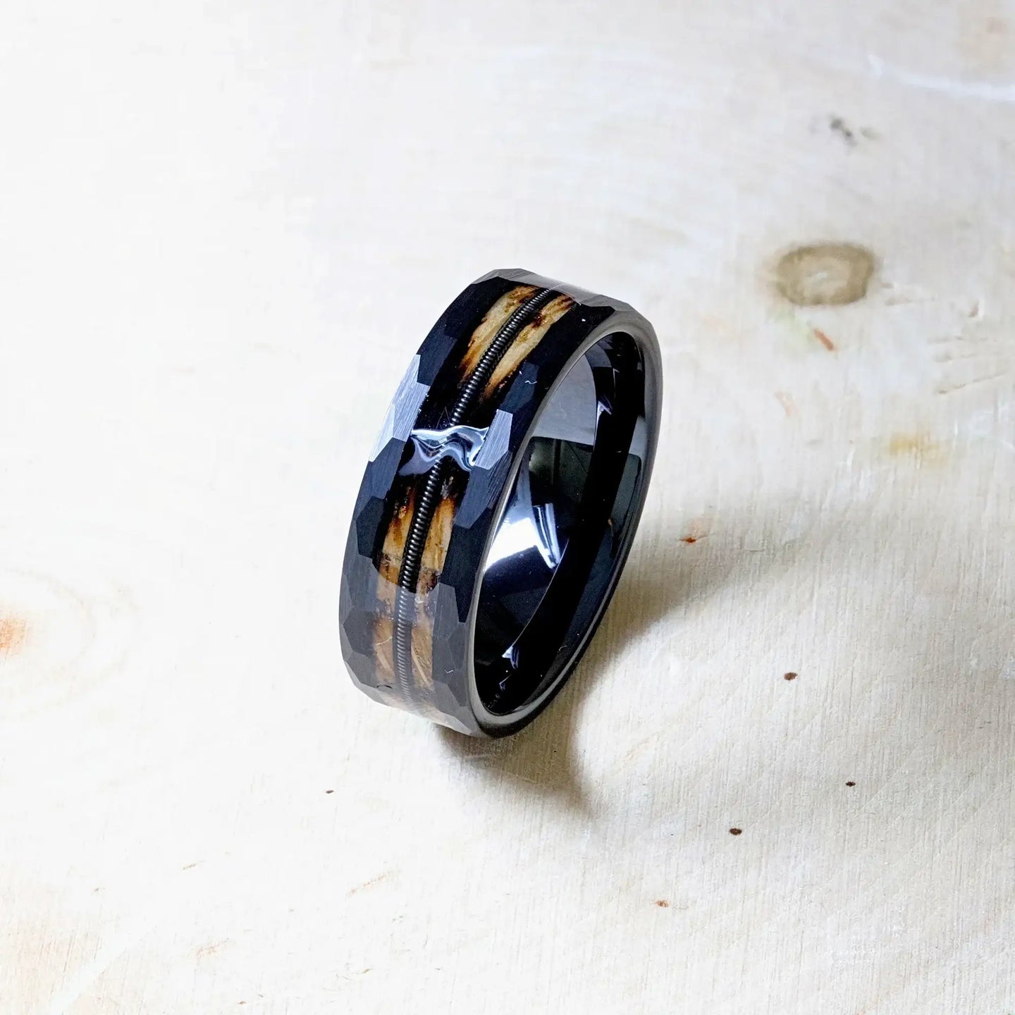 Angled tabletop shot of the ring with glossy black interior, wood inlay, and guitar string