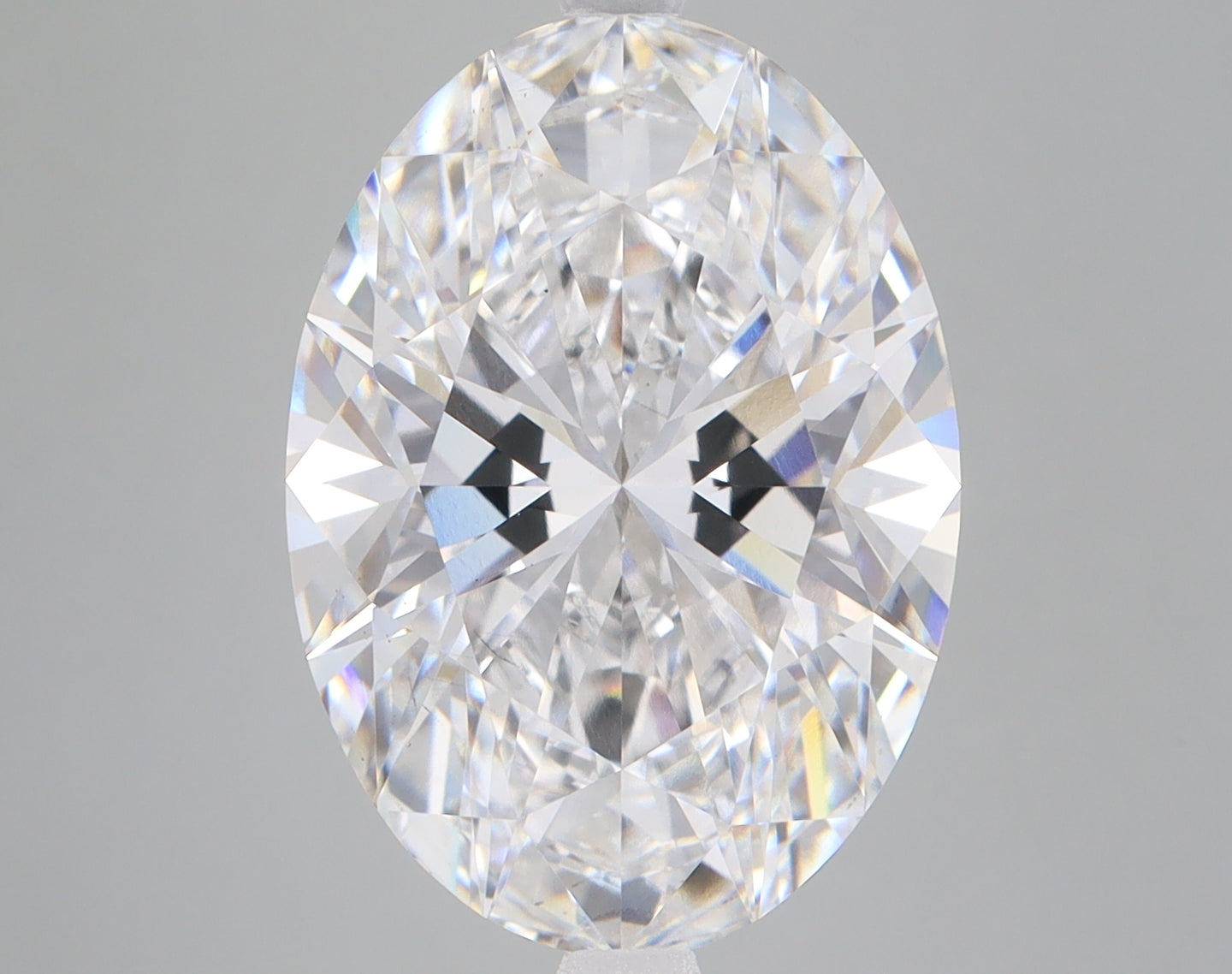 Oval-cut lab-grown diamond with faceted surface reflecting light in multiple colors against neutral gray background.