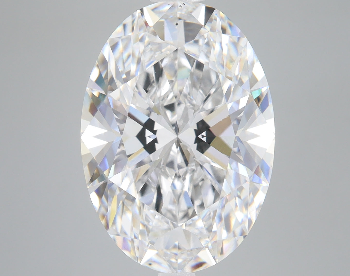 Clear oval-cut diamond with faceted surface and rainbow light refraction on gray background.