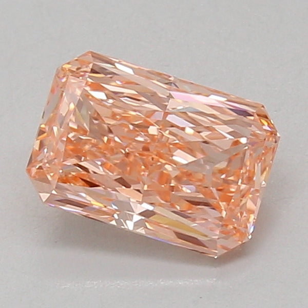 Radiant cut lab grown diamond with peachy-pink hue and faceted surfaces, displayed against neutral background.