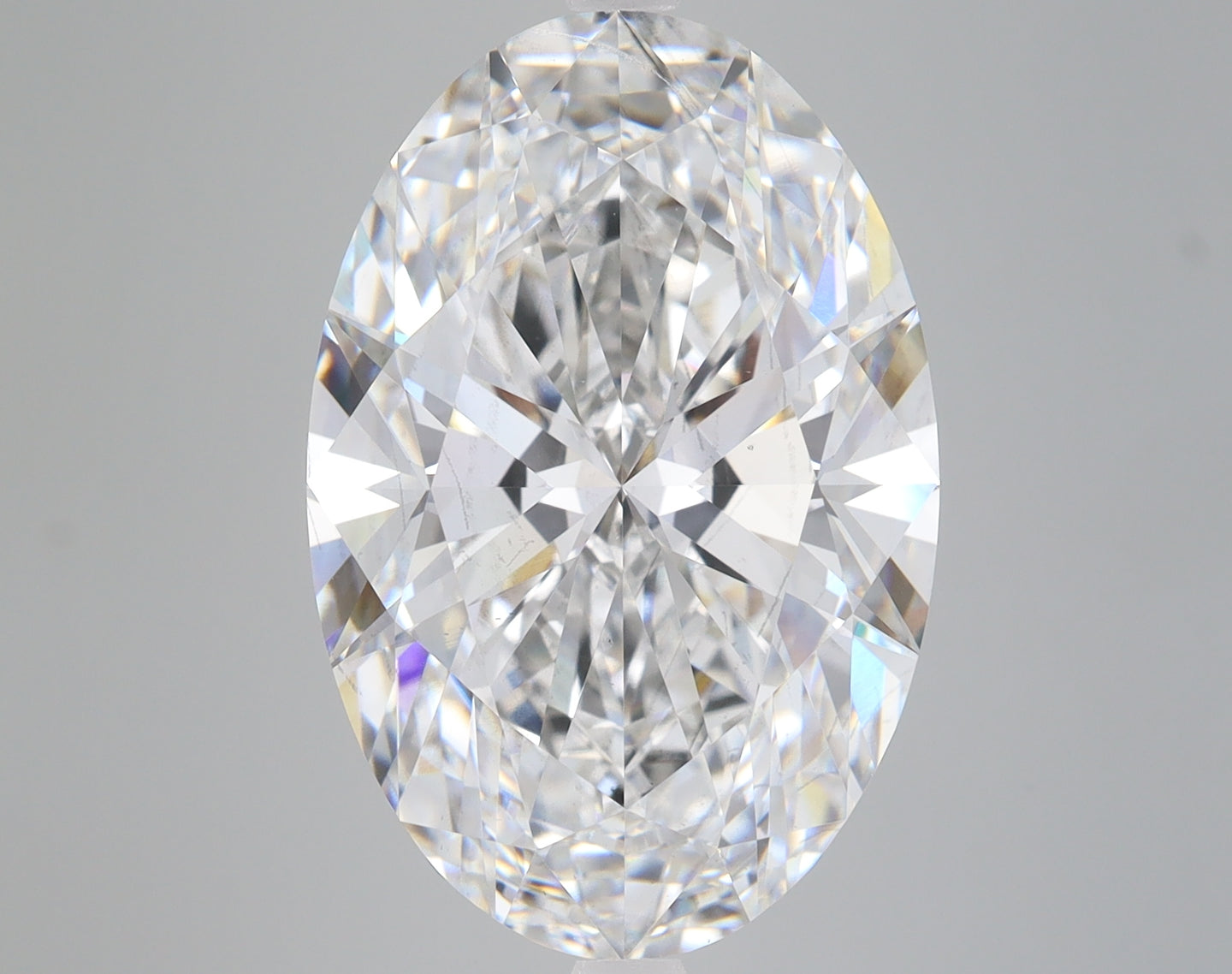 Oval-cut lab-grown diamond with faceted surfaces reflecting light in clear and rainbow tones against gray background.