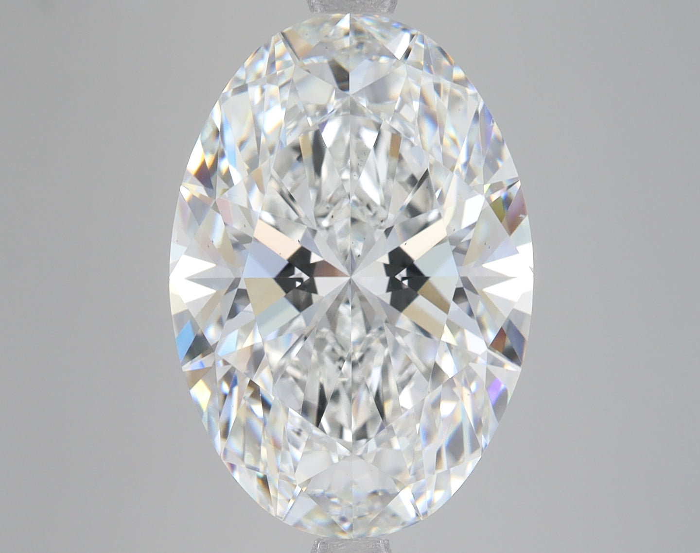 Oval-cut clear lab-grown diamond displaying faceted surface with light refraction, shown against neutral gray background.