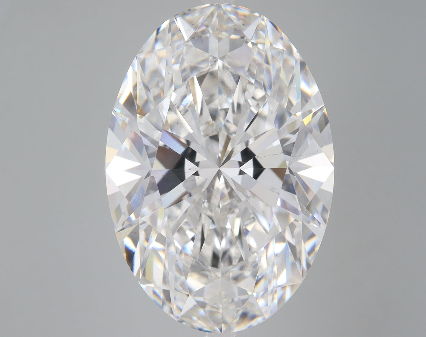 Clear oval-cut lab-grown diamond with faceted surfaces reflecting light, displayed against neutral gray background.