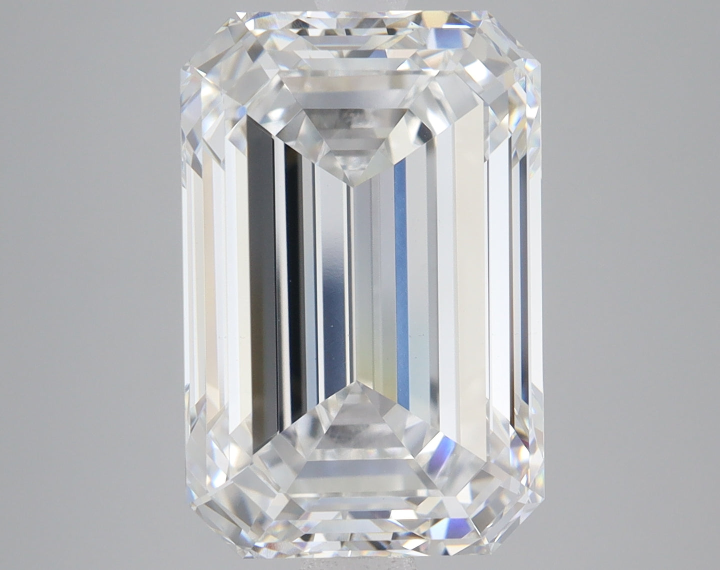 Clear rectangular cut lab-grown diamond loose stone with faceted surfaces reflecting light, displayed against neutral gray ba