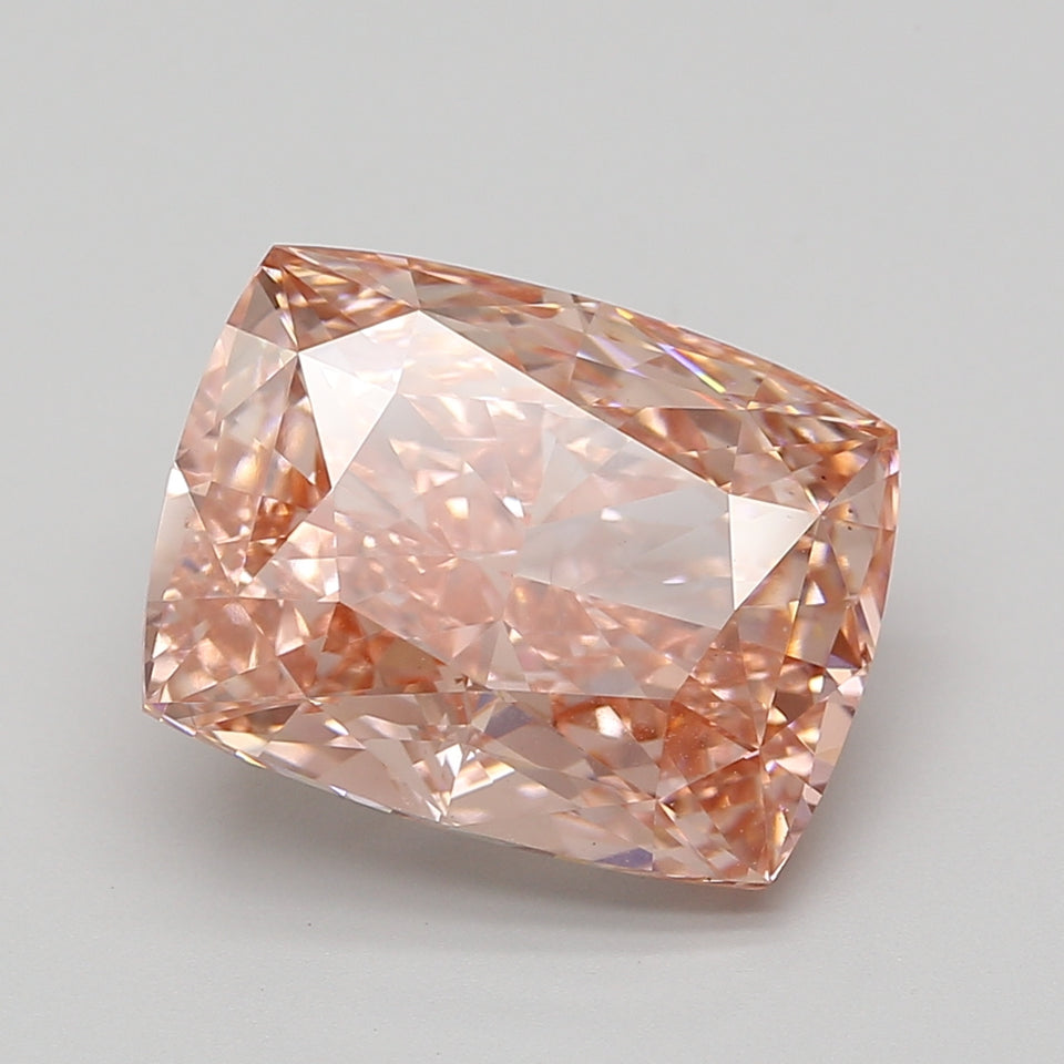 Cushion-cut lab-grown diamond with peachy-pink coloring and faceted surfaces, displayed against a neutral gray background.