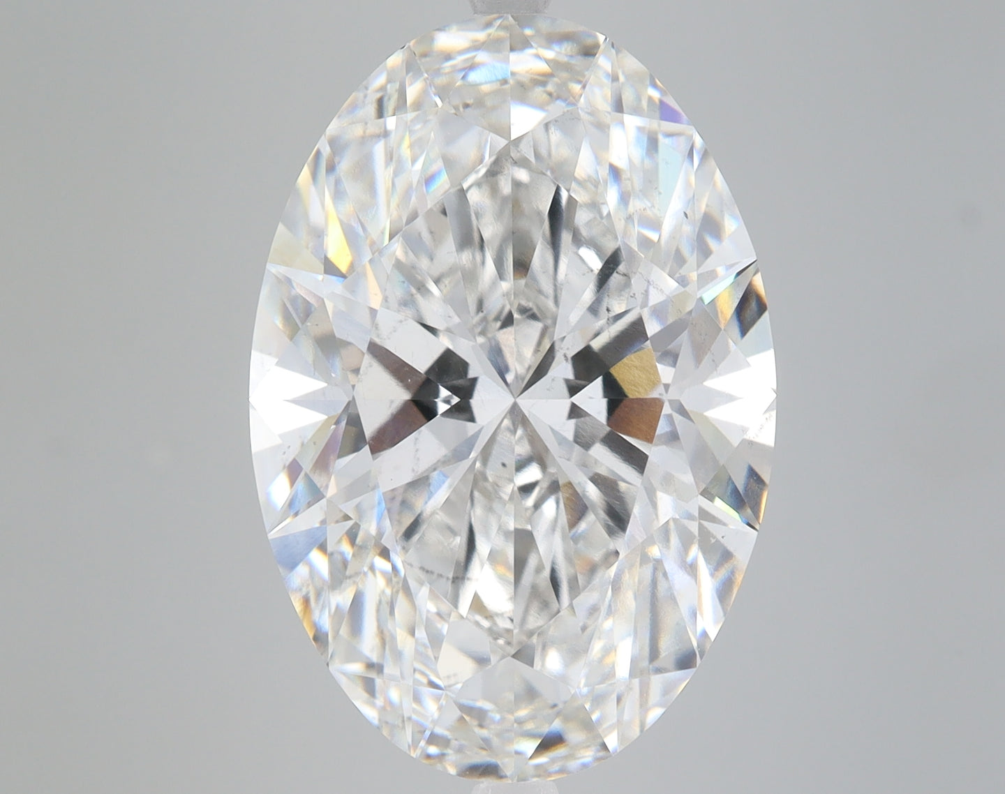 Oval-cut lab-grown diamond with faceted surface displaying light refraction and rainbow sparkle on gray background.