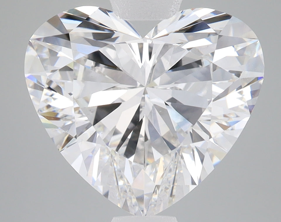 Heart-shaped faceted clear diamond with reflective surfaces on gray background.