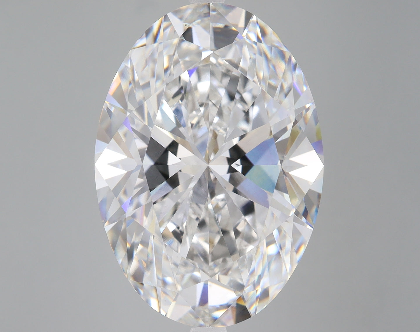 Oval-cut colorless lab-grown diamond with faceted surfaces reflecting light, displayed against neutral gray background.