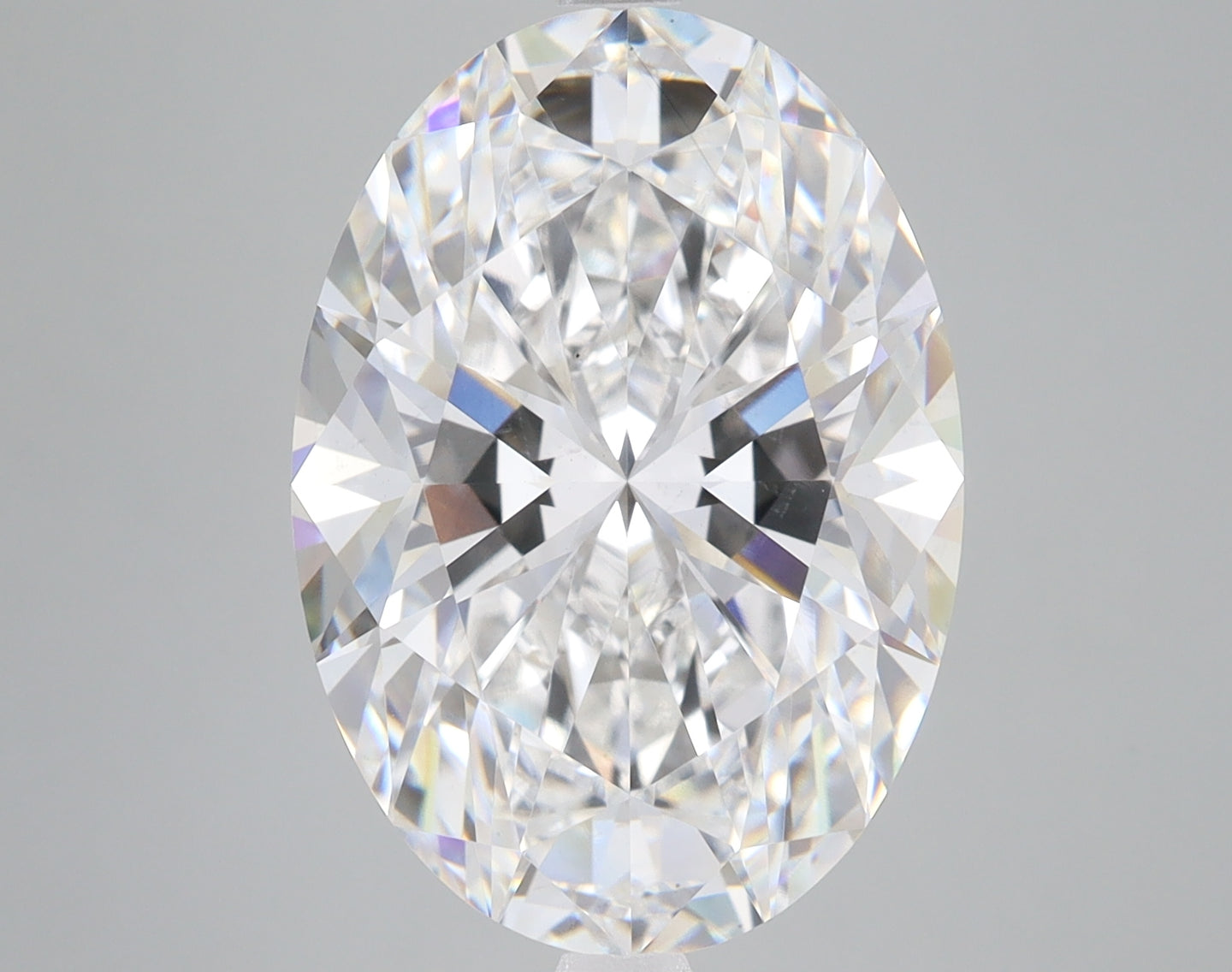 Oval-cut clear diamond with faceted surfaces reflecting light, displayed against a gray background.