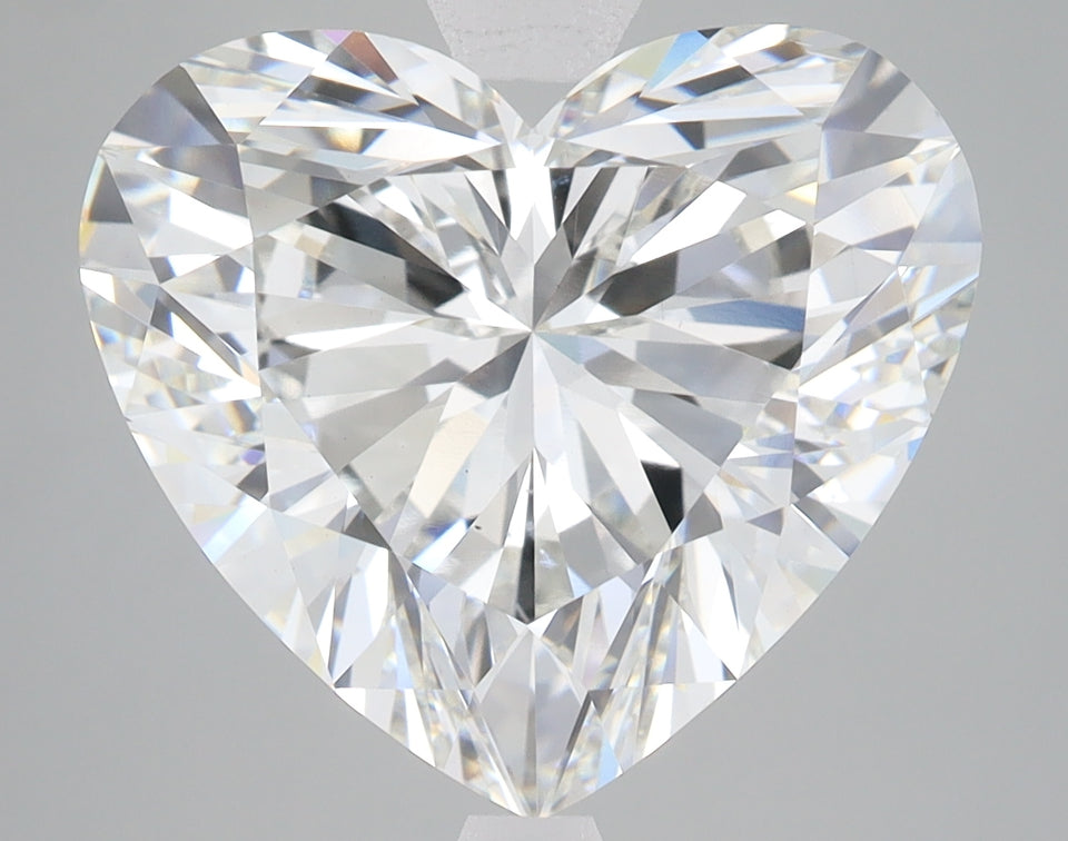 Heart-shaped faceted diamond with brilliant cuts and light reflections displayed against gray background.