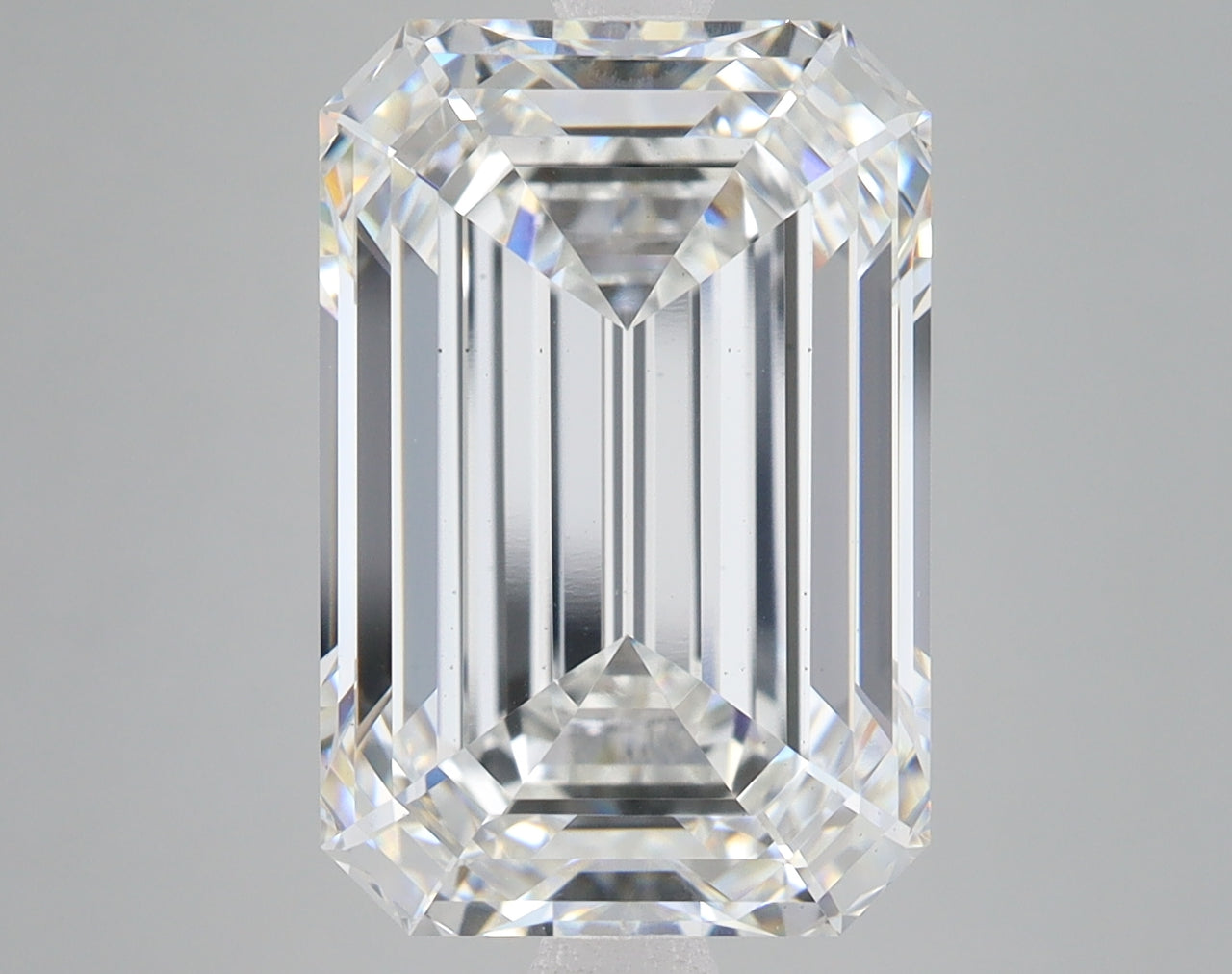 Clear emerald-cut diamond with faceted surfaces and light refraction on neutral gray background.