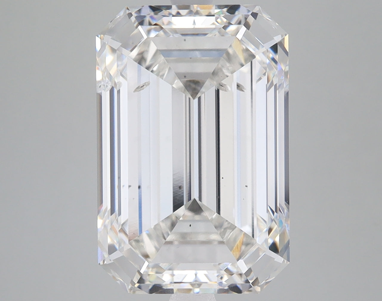 Emerald-cut lab-grown diamond with faceted edges and clear transparency, displayed against neutral gray background.