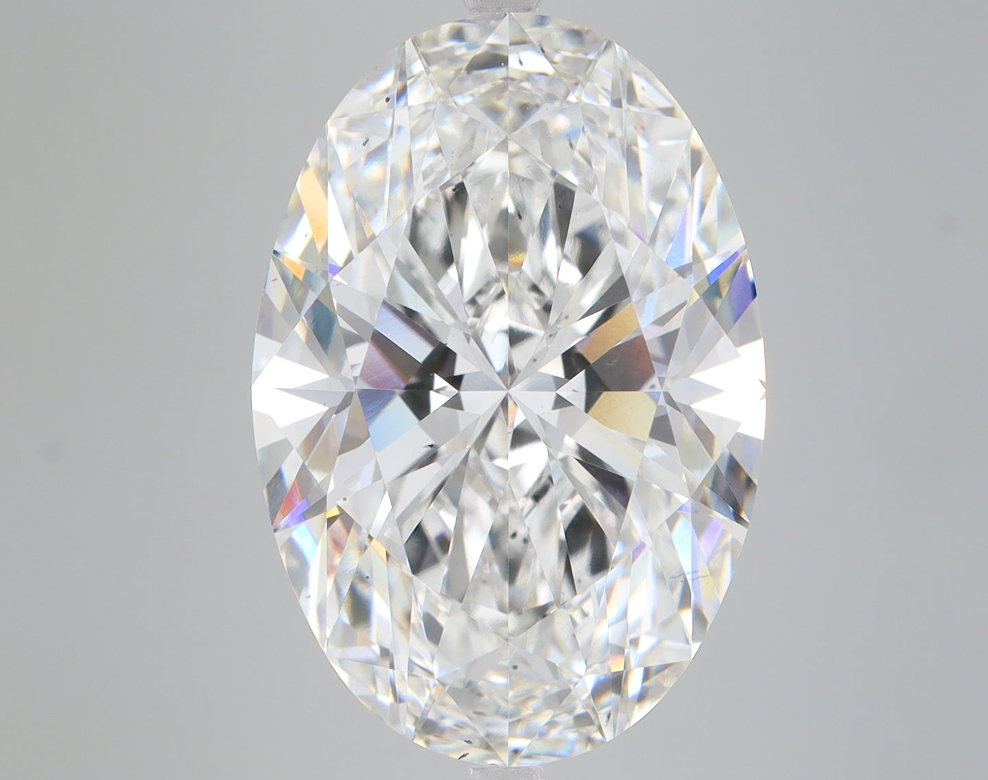 Clear oval-cut diamond with faceted surfaces reflecting light in various colors against a gray background.