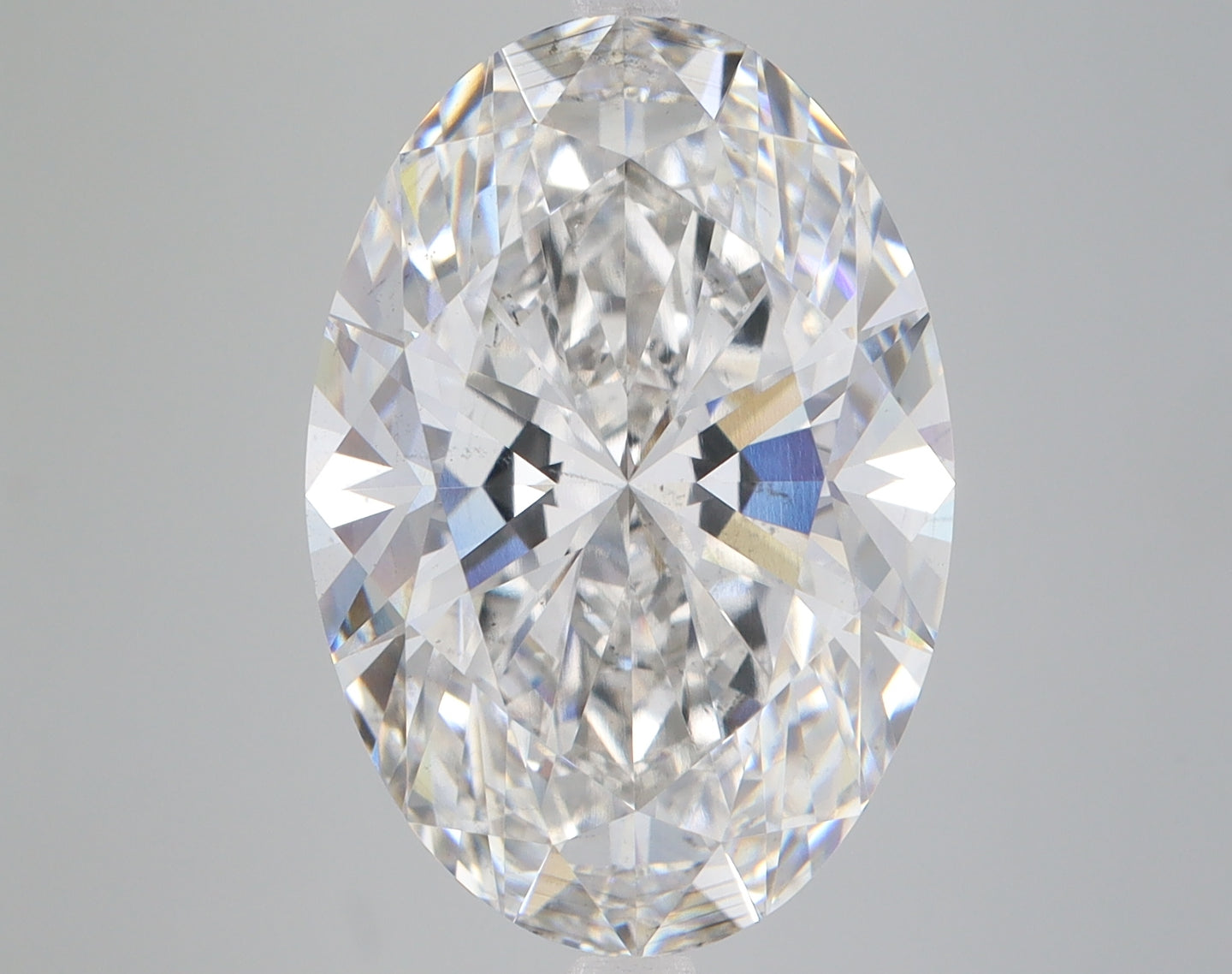 Clear oval-cut lab-grown diamond with faceted surface reflecting light, displayed against neutral gray background.