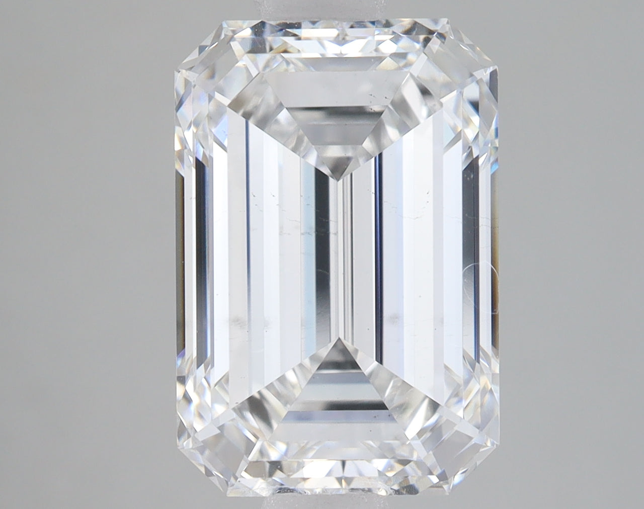 Emerald-cut clear diamond stone with faceted sides and beveled edges, displaying light refraction on neutral background.