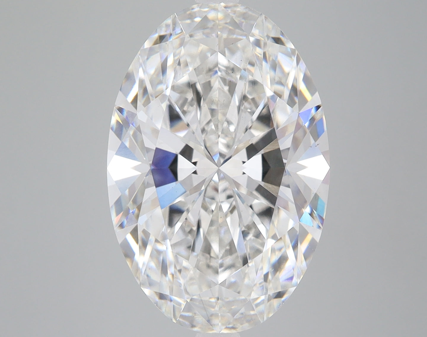 Oval-cut colorless diamond with faceted surface reflecting light, displayed against a neutral gray background.