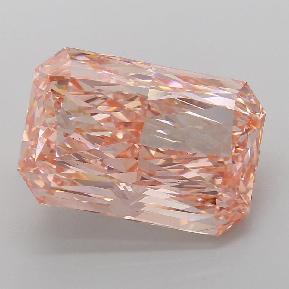 Radiant cut lab grown diamond with peachy-pink hue and faceted surfaces reflecting light, displayed against neutral backgroun